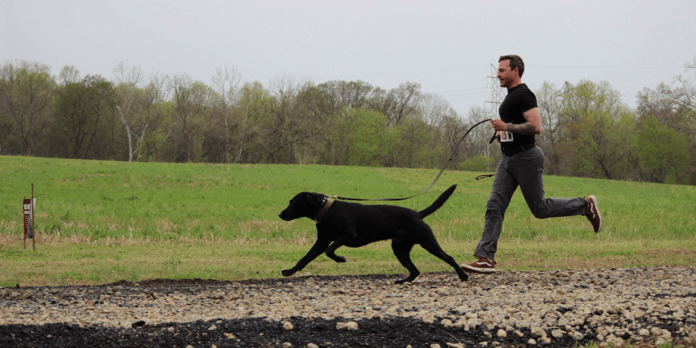 Photo of a person and a dog running on a trail.