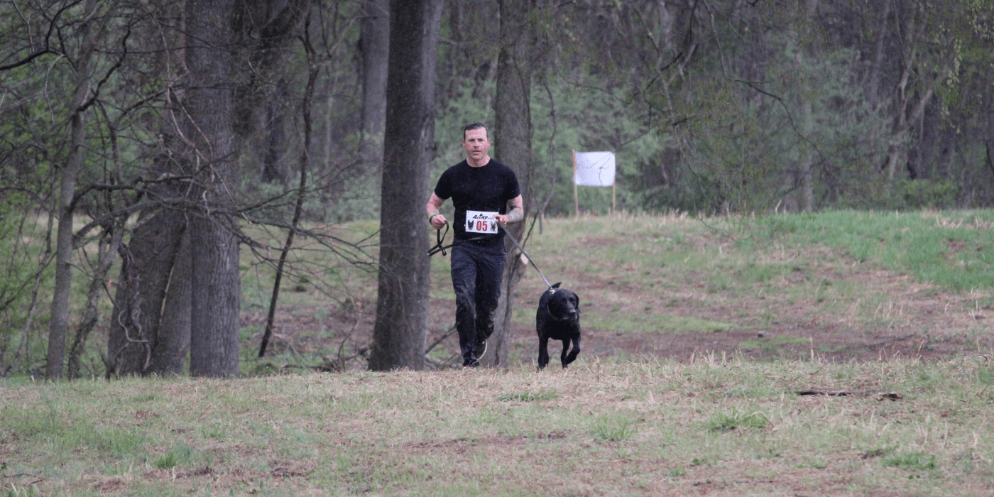 Photo of a person and a dog runing in a field.
