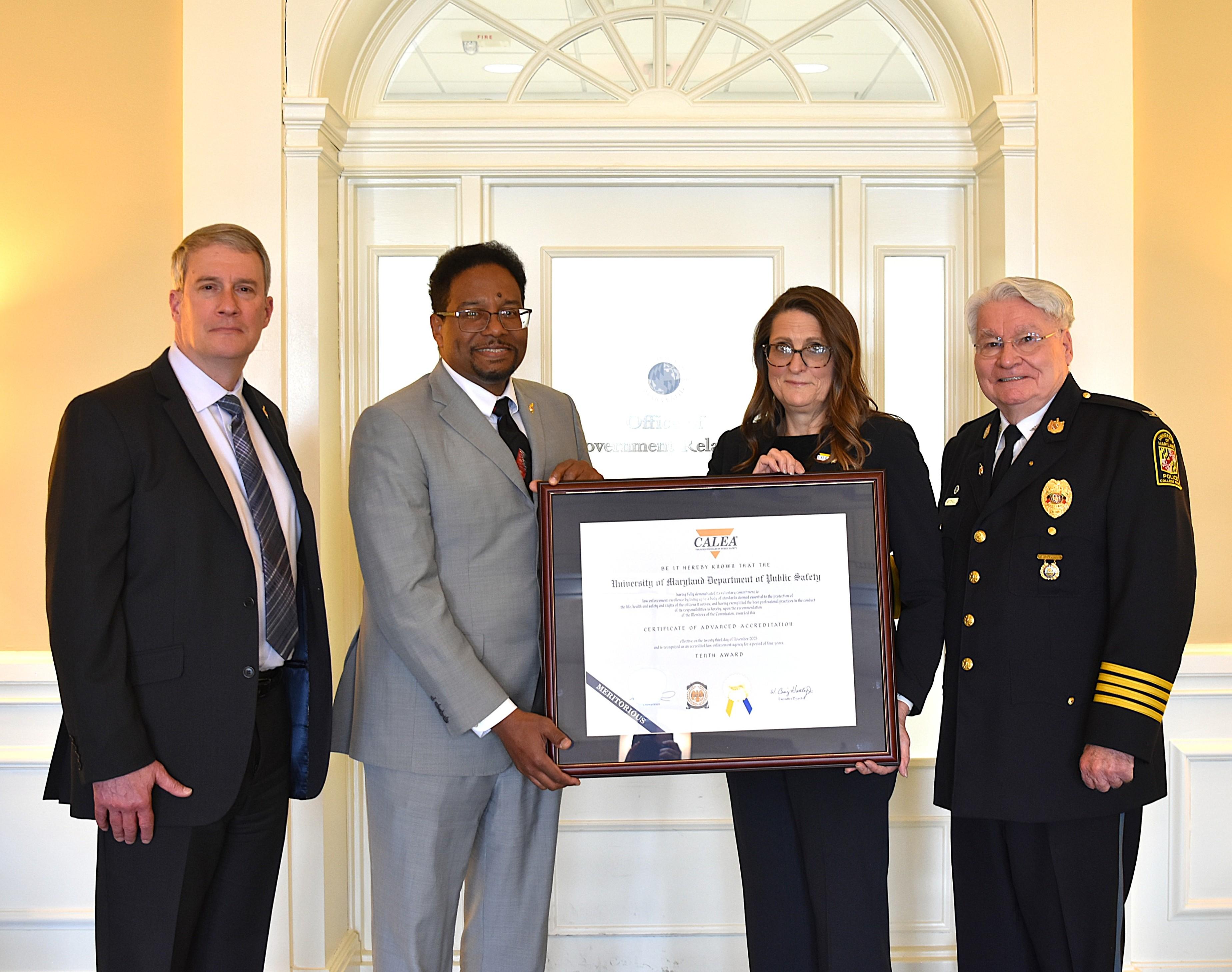 Four people standing for a photo. Two people in the center of the photo are holding a framed award.
